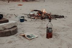 a bottle of alcohol sitting on top of a sandy beach next to a campfire