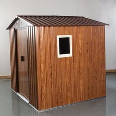 a small wooden storage shed with a window on the front and side door, in an empty room