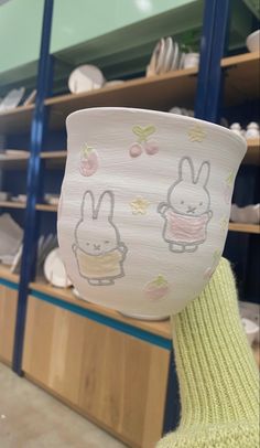 a person holding up a paper cup with drawings on it in front of some shelves