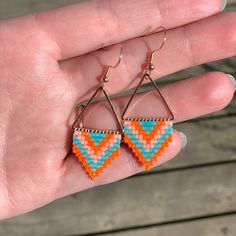 a hand holding a pair of earrings in it's left hand, with an orange and blue triangle design