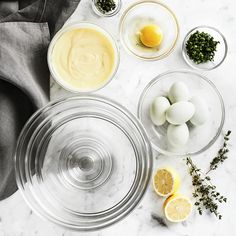 an assortment of ingredients are shown in bowls on a marble countertop, including eggs and lemons