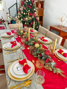 the table is set for christmas dinner with red and gold place mats, silverware, candlesticks, and a tree