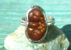 This lovely handmade ring features a natural Fire Agate stone, from the Deer Creek Mine in Arizona. The Fire Agate looks brown in the shade, but in the sun it displays rainbow iridescence and reveals an botryoidal (bubbly) interior structure. The band of the ring is Sterling Silver, and the stone is set with lead free silver bearing solder. Designed and handmade by Clare Thanhauser, one of a kind. 100% natural untreated Fire Agate Size 6 3/4 16 x 9 mm Fire Agate 3mm width of Sterling band Questions welcome! Artisan Brown Gemstone Rings, Oval Brown Agate Rings, Brown Oval Agate Rings, Adjustable Brown Gemstone Rings, Adjustable Oval Rings In Brown, Handmade Oval Brown Rings, Adjustable Oval Brown Rings, Handmade Brown Oval Ring, Oval Brown Ring With Natural Stones