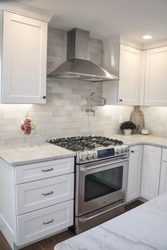 a kitchen with white cabinets and marble counter tops, stainless steel range hood over the stove