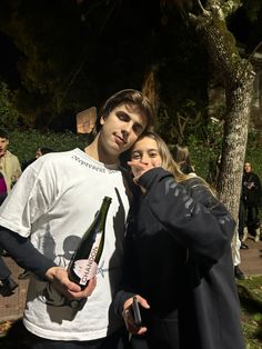 a man and woman standing next to each other holding wine bottles in front of them