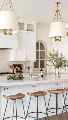 a kitchen island with four stools in front of it and three lights hanging from the ceiling