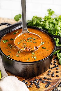 a spoon full of soup sitting on top of a wooden cutting board next to an avocado