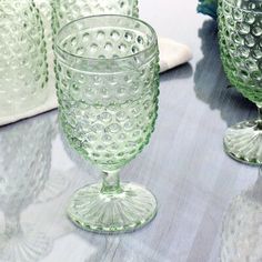 three green glass goblets sitting on a table next to other glasses and napkins