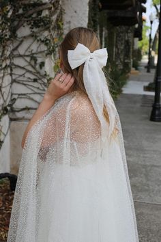 a woman wearing a white veil with a big bow on it's head is walking down the street