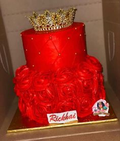 a red cake decorated with roses and a crown on top is sitting in a box