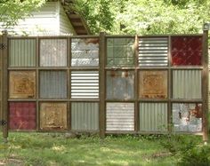 a fence made out of old windows in the grass with trees and bushes behind it