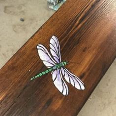 a dragonfly is sitting on top of a piece of wood that has been painted white and green