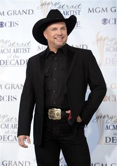 a man in a black suit and cowboy hat smiles at the camera while standing on a red carpet