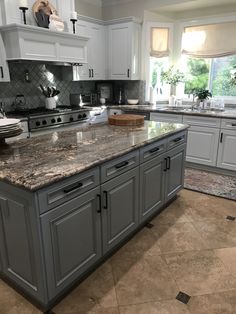 a large kitchen with marble counter tops and white cabinets, along with an island in the middle