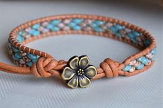 a close up of a bracelet with a flower on the front and an orange cord