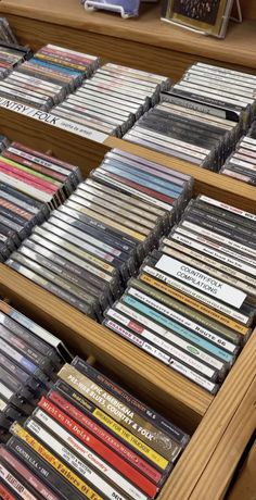 several rows of cds are stacked on top of each other in a wooden shelf next to an open bookcase