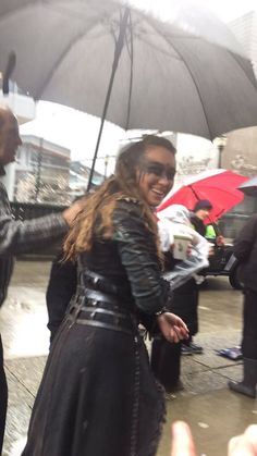 a woman standing under an umbrella in the rain with her hand out to someone else