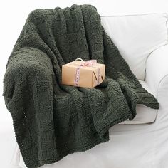 a green blanket sitting on top of a white couch next to a wrapped present box