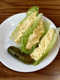 two lettuce halves and a pickle on a white plate with a wooden table