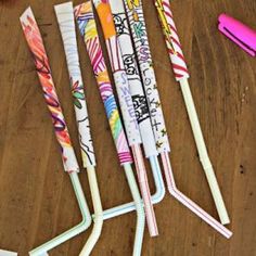 four pens are lined up on a wooden table next to a notebook and pen holder