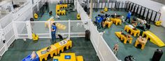 people are standing around in a large building with yellow tables and benches on the floor