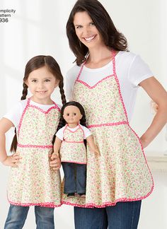 two girls in aprons standing next to each other with a doll on their lap