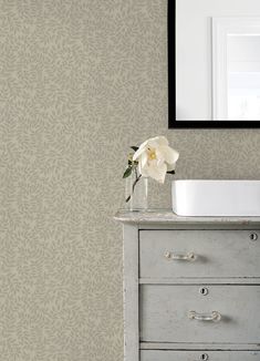 a white flower sitting on top of a dresser in front of a wallpapered bathroom