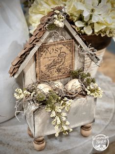 a bird house with some flowers in front of it and an old postcard on the roof