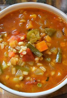 a white bowl filled with vegetable soup on top of a wooden table next to a spoon