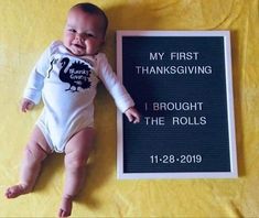 a baby laying next to a sign that says, my first thanksgiving i brought the rolls