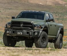 a large green truck parked on top of a grass covered field next to a hill