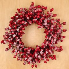 a wreath made out of red berries on a wooden surface with the word merry written below it