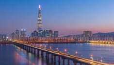 the city skyline is lit up at night with lights reflecting off the water and bridge