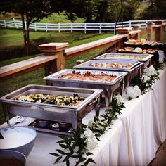 a table with many trays of food sitting on top of it next to a fence