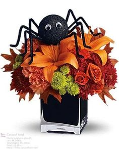 a spider bouquet with orange and green flowers in a black square vase on a white background