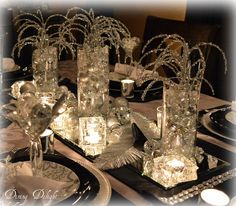 the table is set with clear glass vases and silver candlesticks on black plates