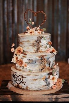 a three tiered cake with flowers on the side and a heart at the top