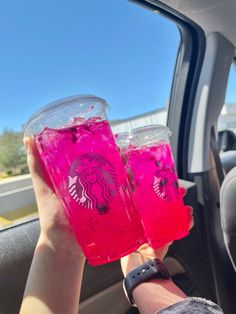 two people holding up pink drinks in the back seat of a car