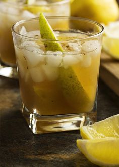 two glasses filled with lemonade and limes on a wooden table next to sliced lemons