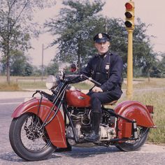 a man riding on the back of a red motorcycle next to a traffic light at an intersection