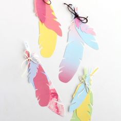 four different colored feathers with string attached to them on a white surface, one is pink, the other is blue and yellow