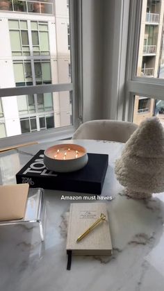 a table topped with a book and a bowl filled with candles next to a window