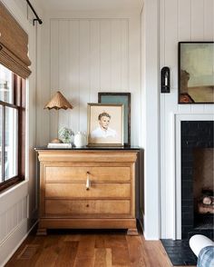 a living room with a fireplace and pictures on the wall, along with a wooden dresser