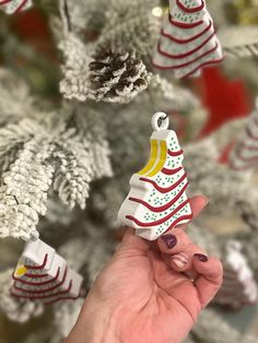 a hand holding a small christmas tree ornament in front of a decorated christmas tree