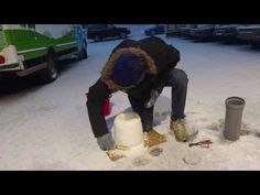 a man kneeling down in the snow next to a trash can