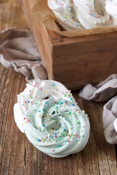 cupcakes with white frosting and sprinkles are on a wooden table