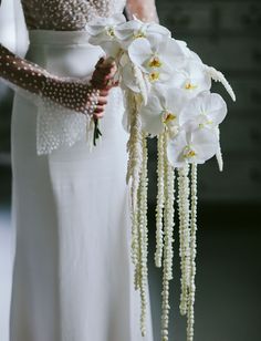 a woman in a white dress holding a bouquet of flowers with pearls on the side