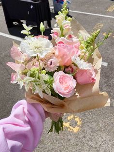 a bouquet of pink and white flowers is held by someone's hand on the street