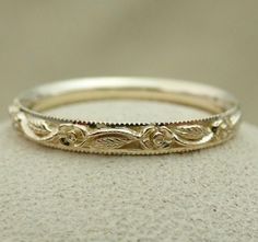 a gold wedding band that is on top of a white stone surface and has an intricate design