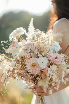 a woman holding a bouquet of white and pink flowers in front of her face with the sun behind her